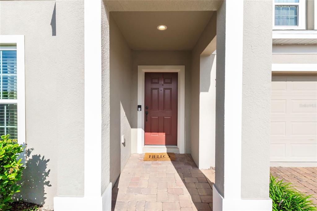 A red front door is centered within a covered entryway with a paved walkway — 9399 VILLANOVA DRIVE, GROVELAND, FL