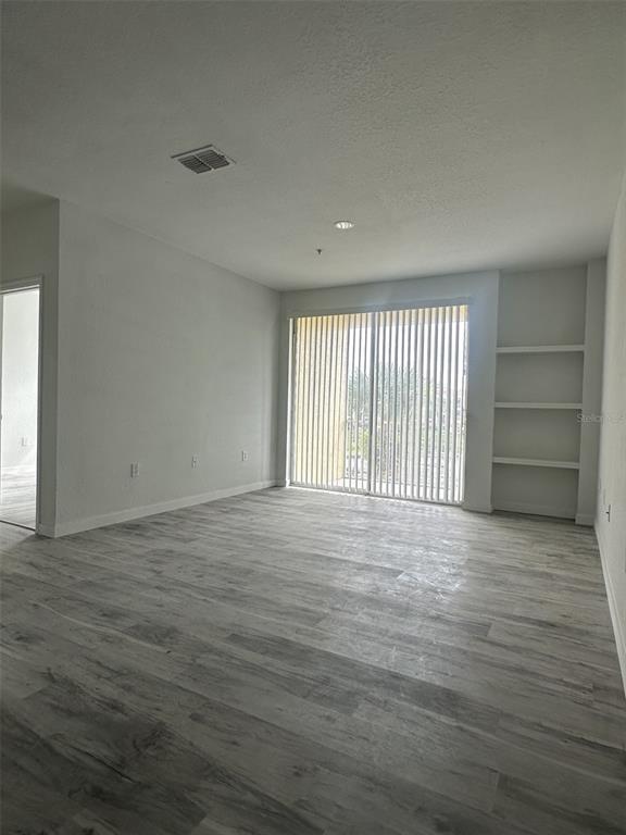 An empty living room features light wood-look flooring, built-in wall shelves, and sliding glass doors — 1175 LAKE SHADOW CIRCLE UNIT 4202, MAITLAND, FL