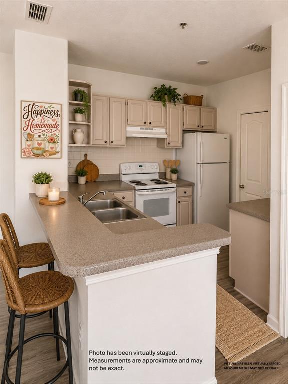 This kitchen features light-colored cabinets, a white stove, a refrigerator, and a breakfast bar — 1175 LAKE SHADOW CIRCLE UNIT 4202, MAITLAND, FL