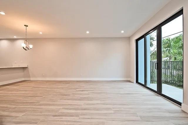 An empty living room with light wood-look tile flooring and a large sliding glass door — FORT LAUDERDALE, FL