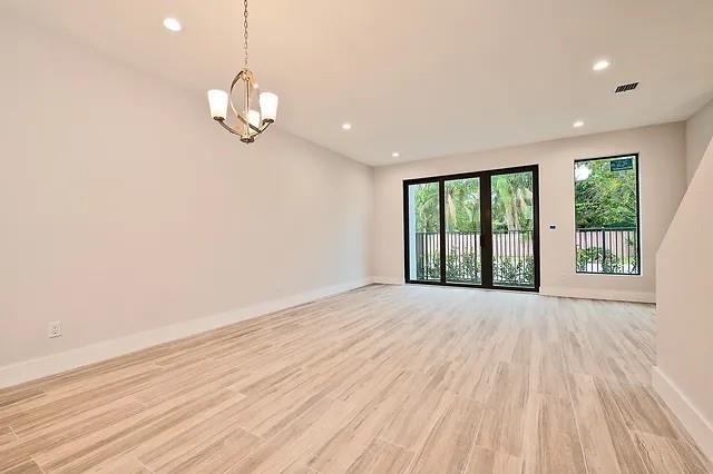 An empty room with light wood-look tile flooring, a chandelier, and large glass sliding doors — FORT LAUDERDALE, FL