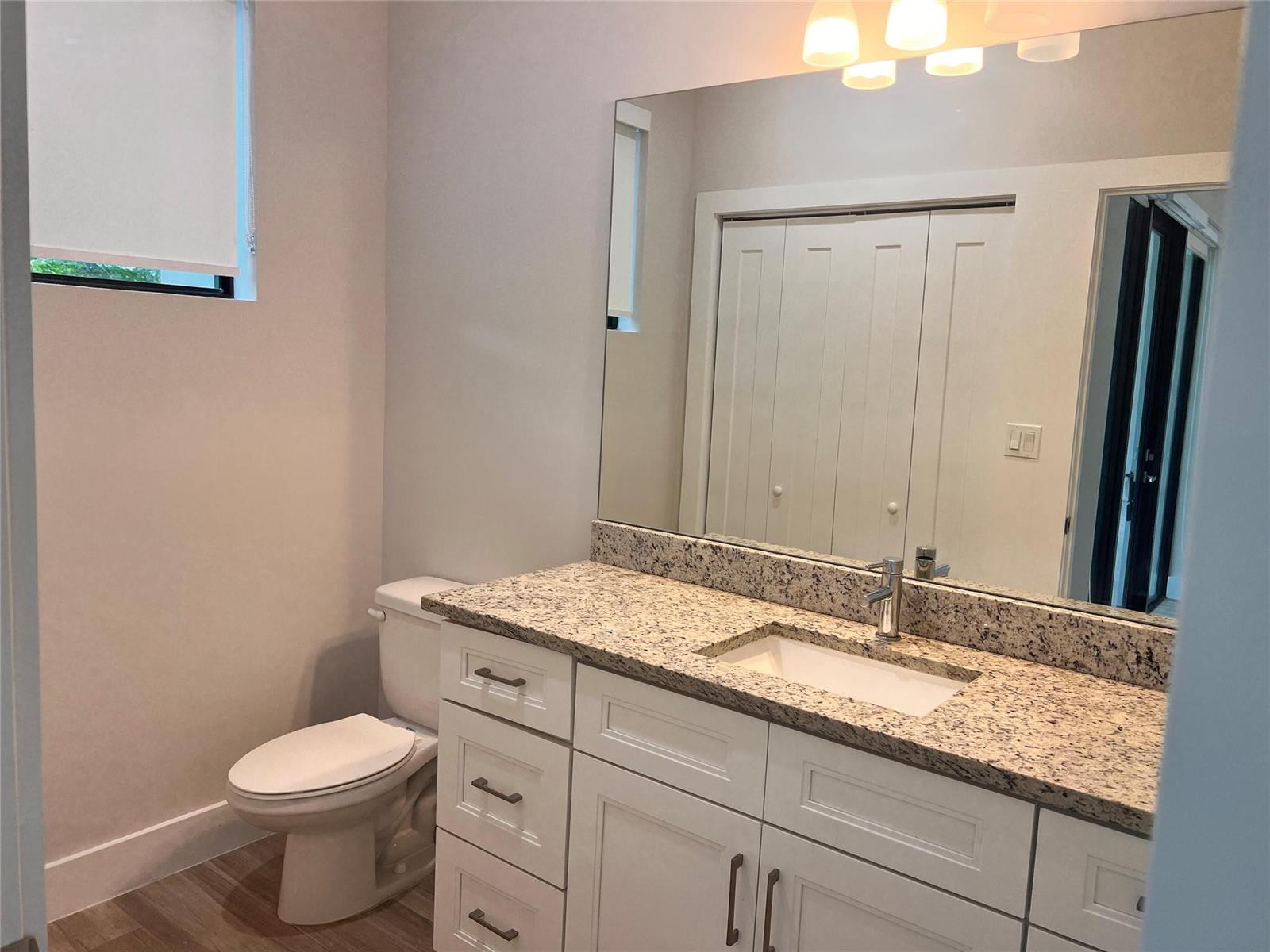 A bathroom features a white vanity with a granite countertop, a mirror, and a toilet — FORT LAUDERDALE, FL