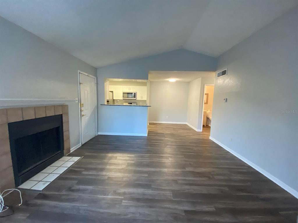 A living room with a fireplace, wood-look flooring, and an open view into the kitchen — 4400 THORNBRIAR LANE UNIT 205, ORLANDO, FL
