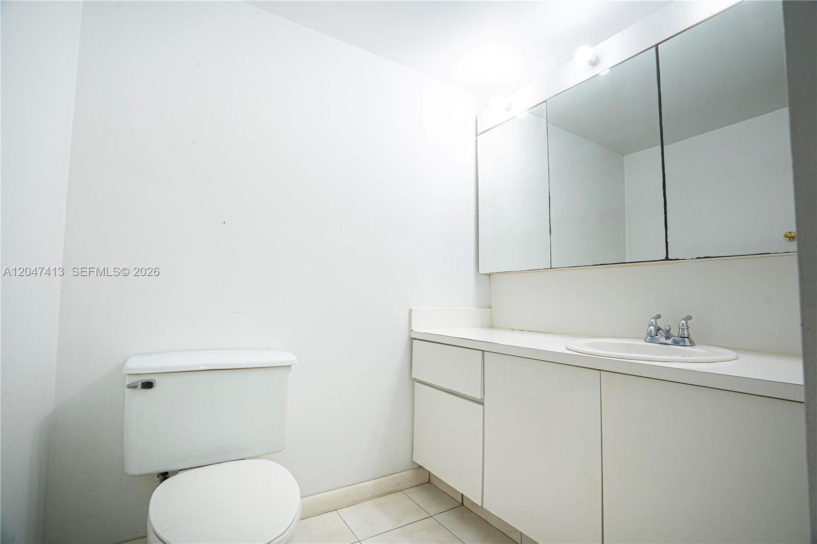 A white bathroom features a toilet, a vanity with a sink, and a mirrored cabinet — 600 Three Islands Blvd # 316, Hallandale Beach FL 33009, HALLANDALE BEACH, FL