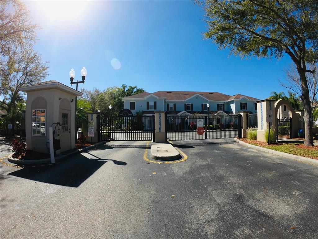 A gated entrance with a guardhouse leads to a two-story residential building under a clear sky — 2954 LUCAYAN HARBOUR CIRCLE UNIT 106, KISSIMMEE, FL