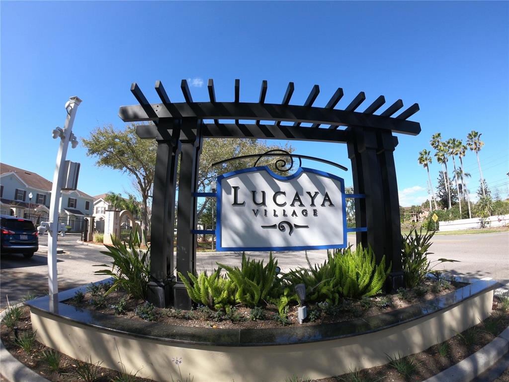 A black pergola structure displays a Lucaya Village sign above a landscaped garden bed — 2954 LUCAYAN HARBOUR CIRCLE UNIT 106, KISSIMMEE, FL