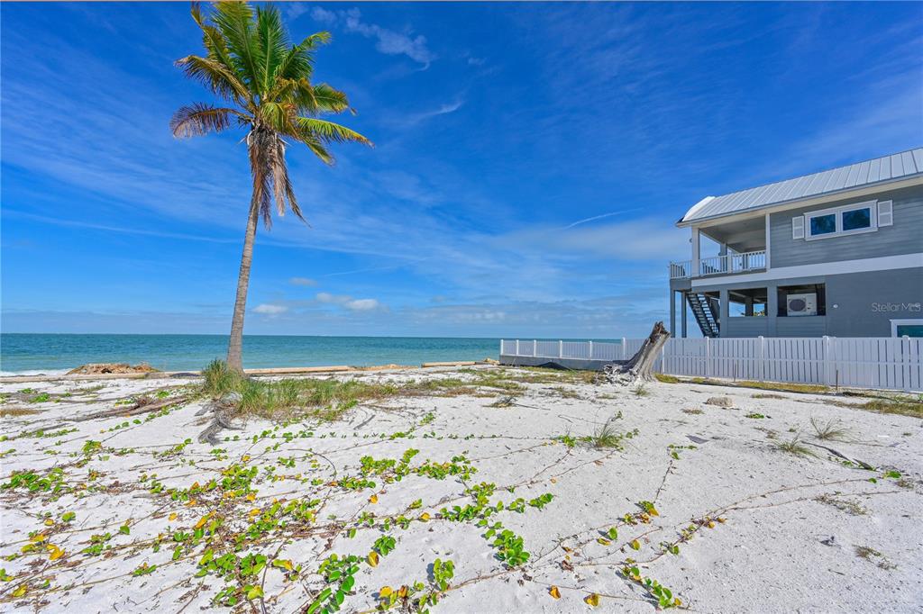 A palm tree stands on a sandy beach next to a house with a fence — 839 N SHORE DRIVE, ANNA MARIA, FL