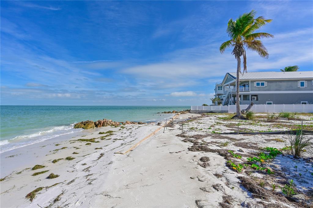 A sandy beach with a palm tree and a multi-story house along the shoreline — 839 N SHORE DRIVE, ANNA MARIA, FL