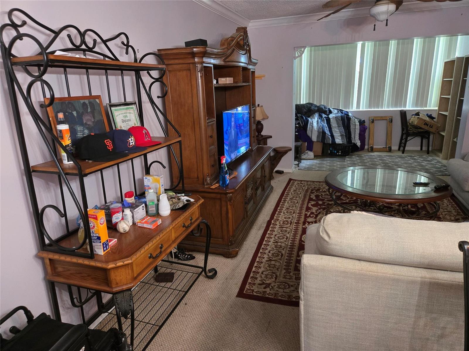 A living room features a wooden entertainment center, a metal shelving unit, and a coffee table — 3080 Holiday Springs Boulevard # 209, Margate FL 33063, MARGATE, FL