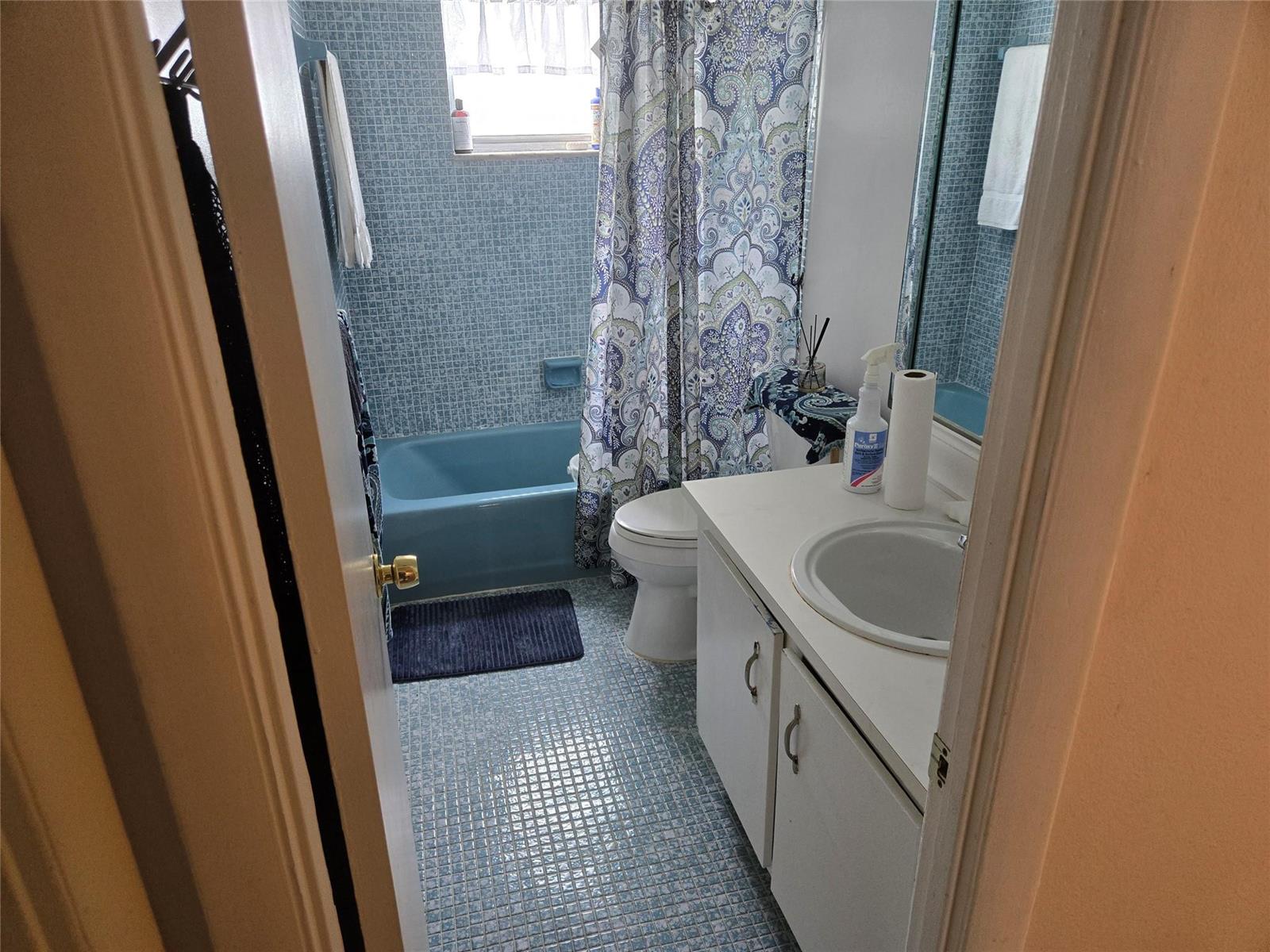 A bathroom features blue mosaic tile, a blue bathtub, a white vanity, and a patterned curtain — 3080 Holiday Springs Boulevard # 209, Margate FL 33063, MARGATE, FL