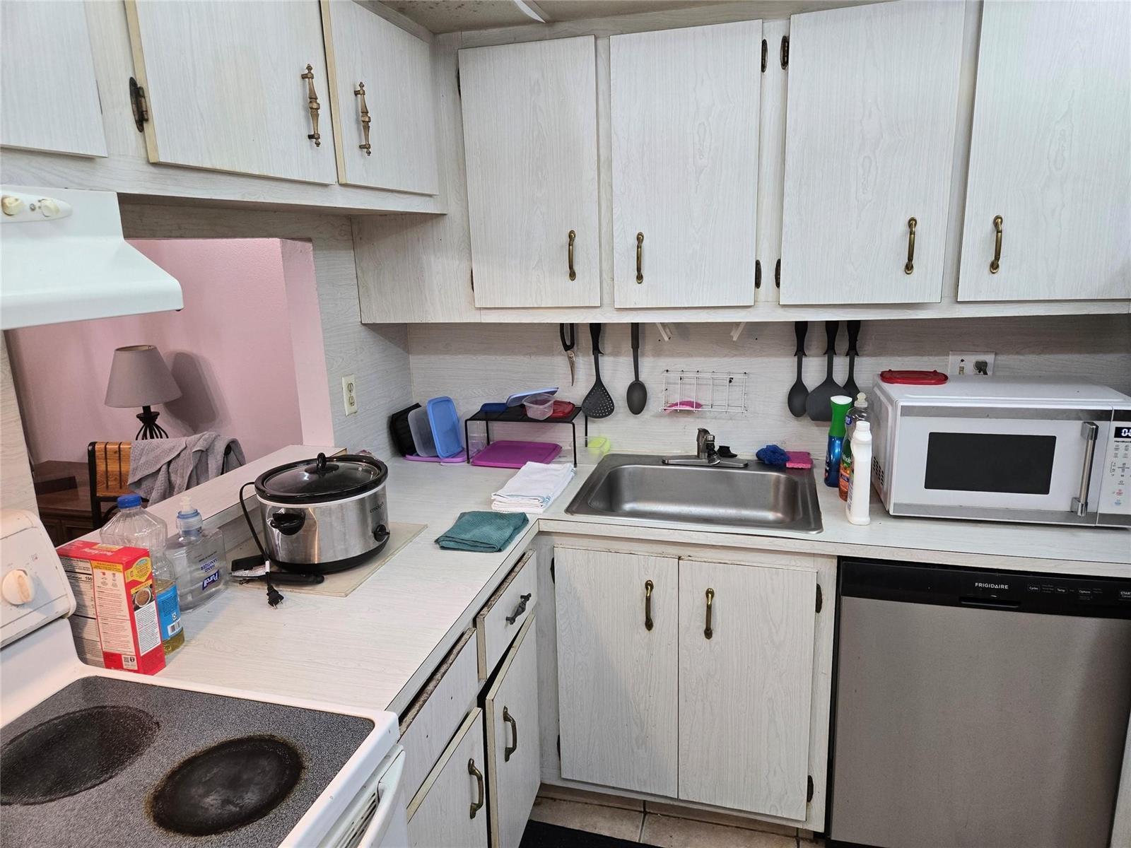 A kitchen features white wood-grain cabinets, a stainless steel sink, and a microwave on the counter — 3080 Holiday Springs Boulevard # 209, Margate FL 33063, MARGATE, FL