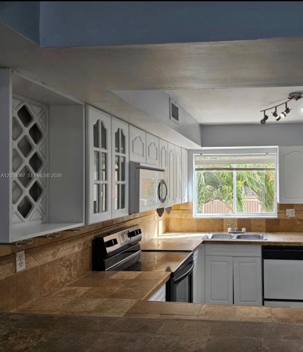 A kitchen features white cabinets, a wine rack, tile countertops, and a window above the sink — 14909 SW 80th St # 205, Miami FL 33193, MIAMI, FL