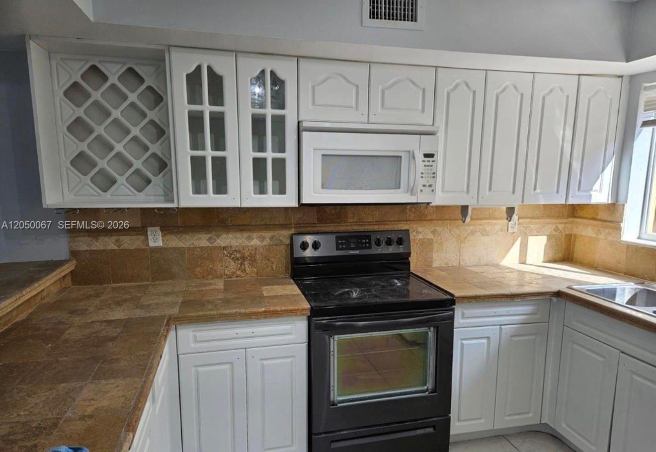 A kitchen features white cabinets, a black stove, a microwave, and tan tile countertops — 14909 SW 80th St # 205, Miami FL 33193, MIAMI, FL