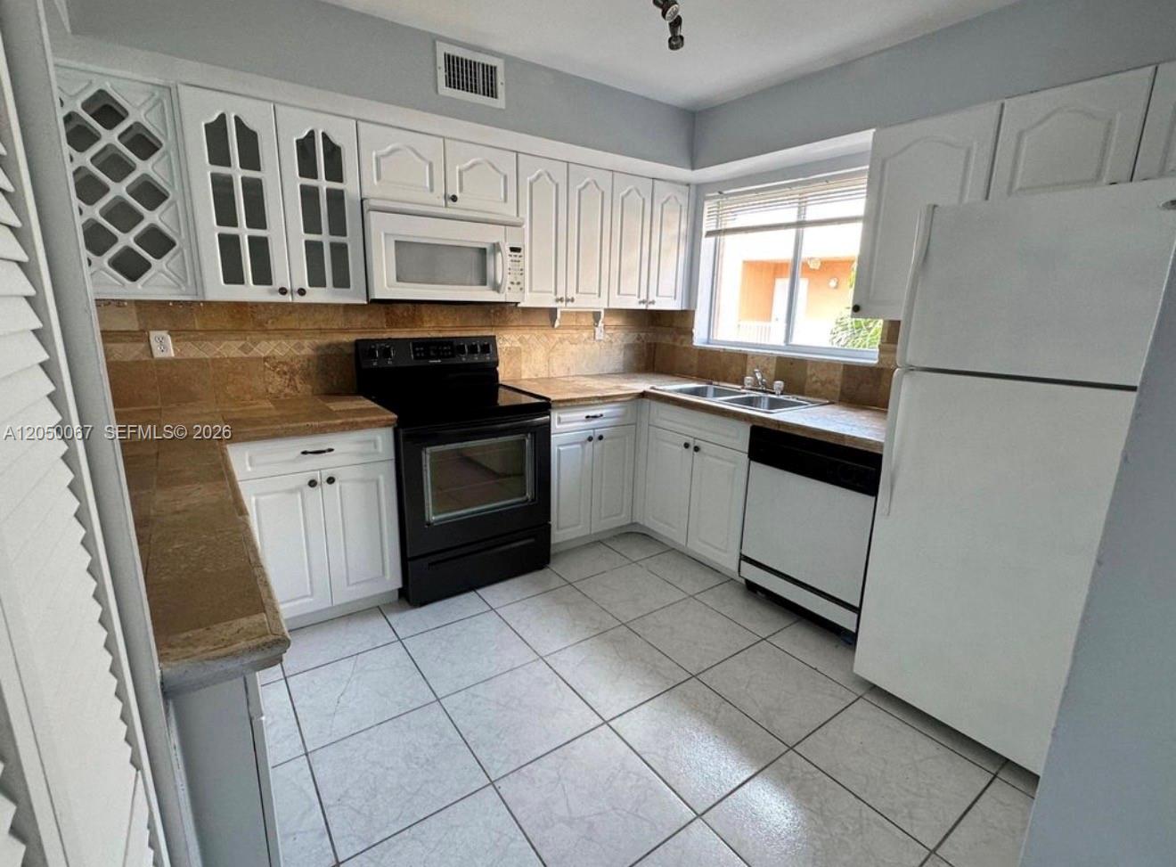 A kitchen features white cabinets, black appliances, tile flooring, and a tan tile backsplash — 14909 SW 80th St # 205, Miami FL 33193, MIAMI, FL