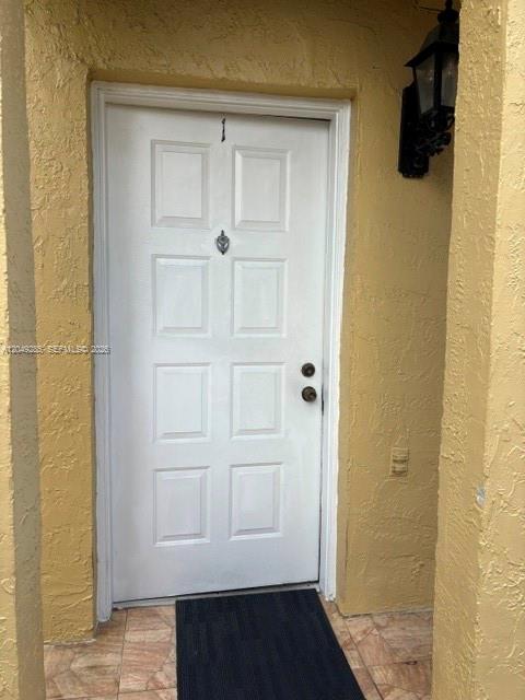 A white front door with a knocker and handle is set in a yellow stucco wall — 415 NW 85th Pl # 1701, Miami FL 33126, MIAMI, FL