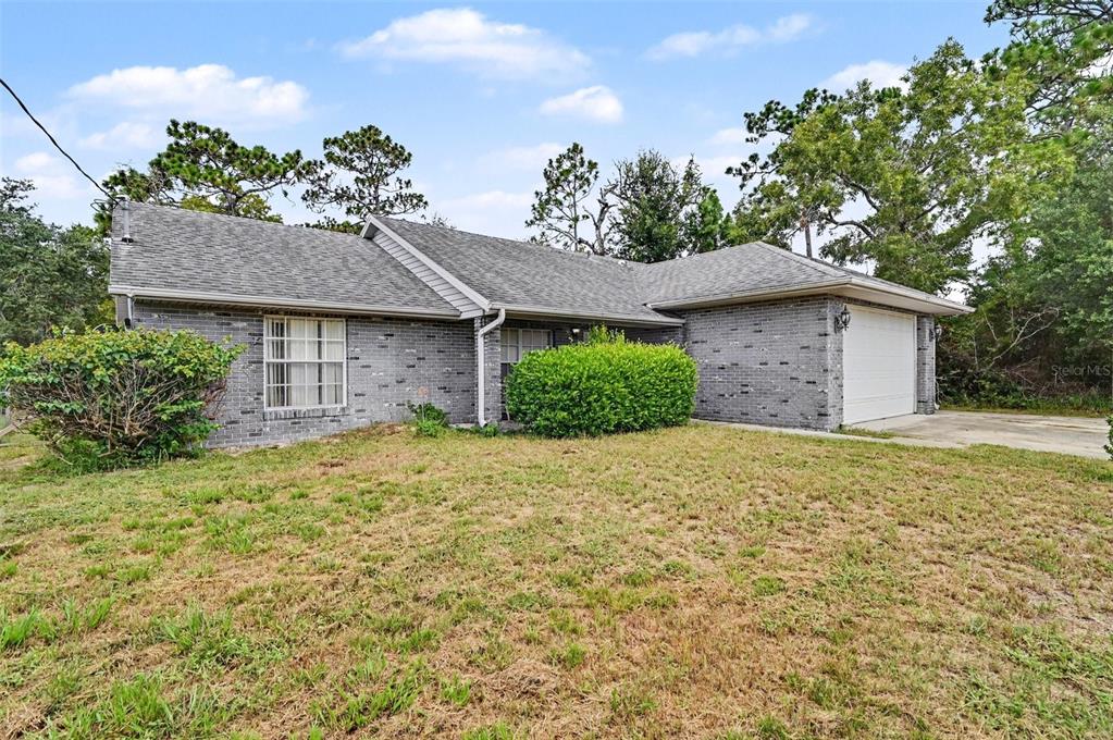 A single-story gray brick house with a shingled roof, attached garage, and front lawn — 1339 LODGE TERRACE, DELTONA, FL