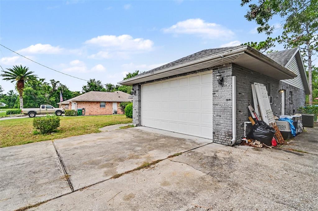 A gray brick garage with a white door sits next to a concrete driveway — 1339 LODGE TERRACE, DELTONA, FL