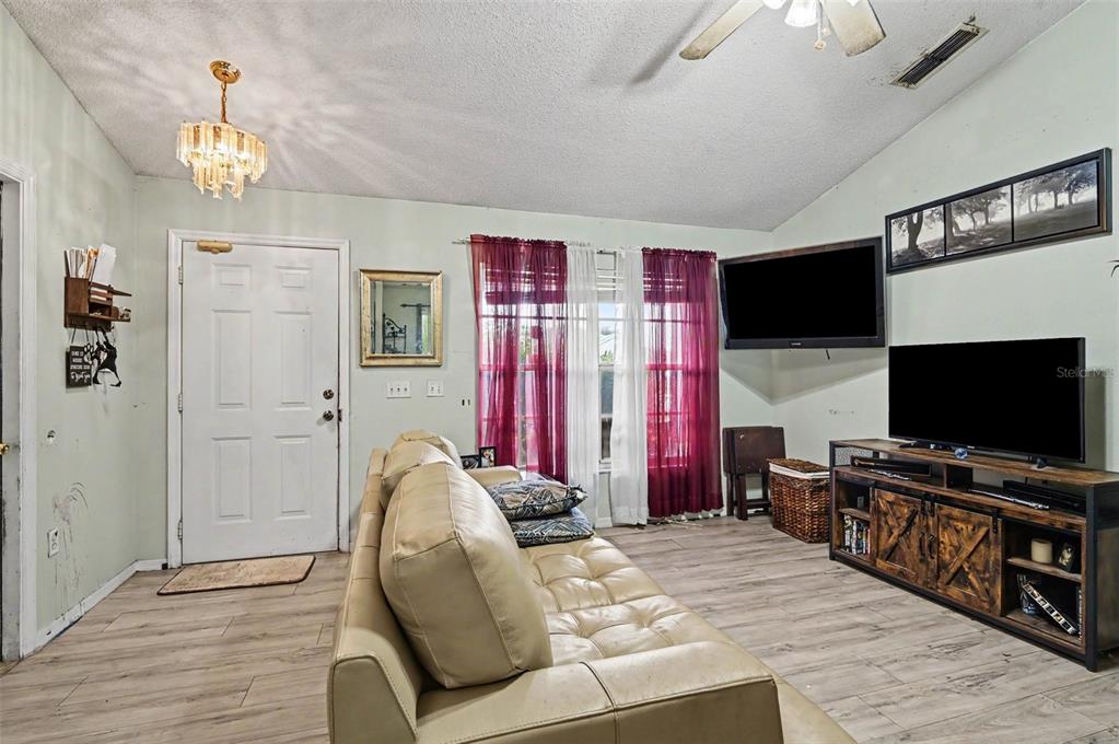 A living room features light wood-look flooring, a beige sofa, and a wall-mounted television — 1339 LODGE TERRACE, DELTONA, FL