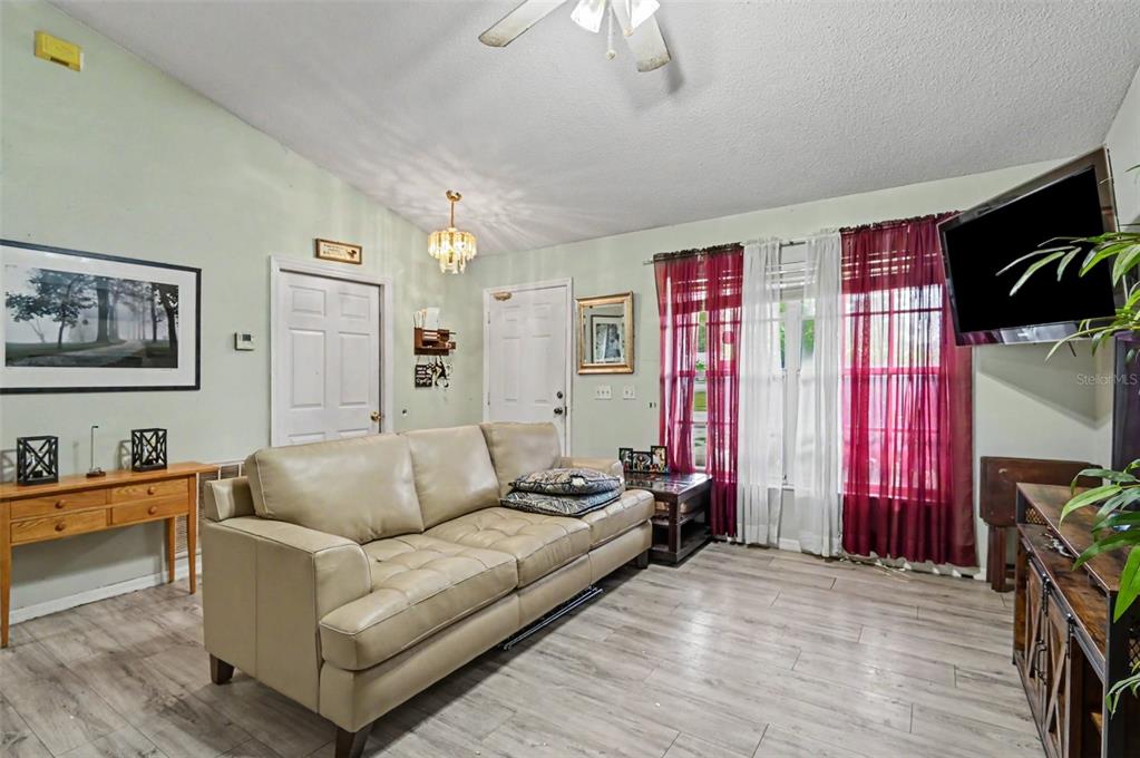A living room features a beige sofa, wood-look flooring, a ceiling fan, and red curtains — 1339 LODGE TERRACE, DELTONA, FL