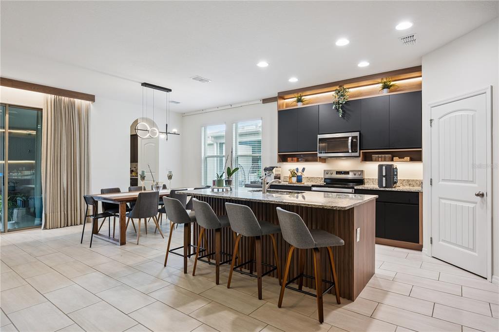 A modern kitchen features dark cabinetry, a large island with bar seating, and an adjacent dining area — 17070 WATER SPRING BOULEVARD, WINTER GARDEN, FL