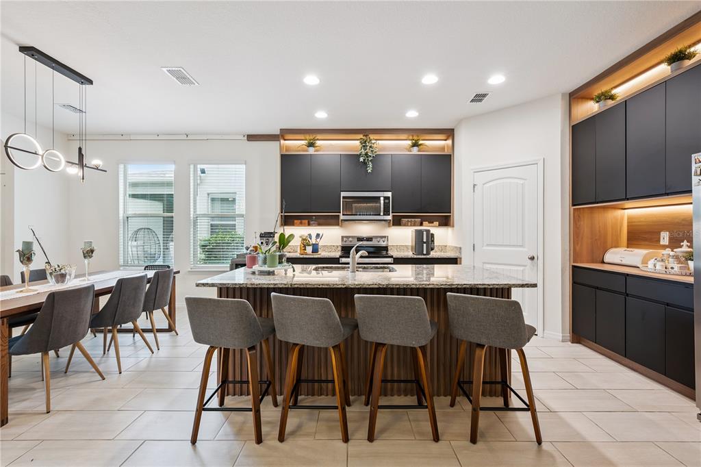 A modern kitchen features dark cabinetry, a granite-topped island with four stools, and an adjacent dining area — 17070 WATER SPRING BOULEVARD, WINTER GARDEN, FL