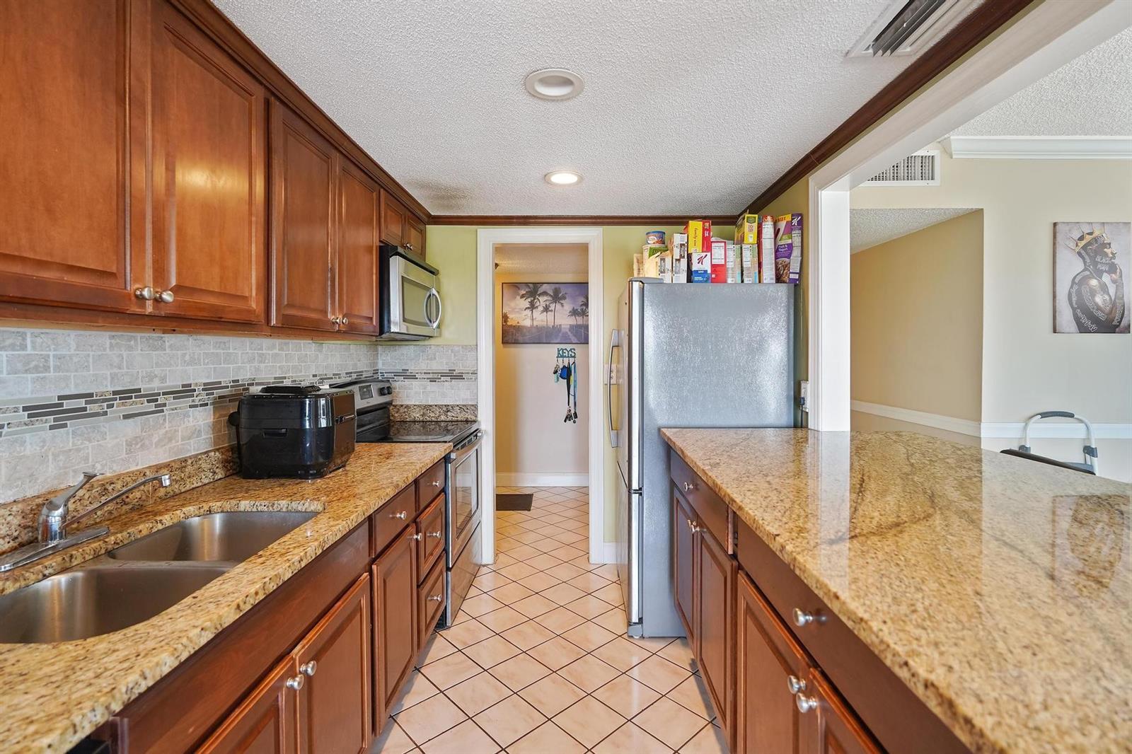 A galley kitchen features wood cabinets, granite countertops, stainless steel appliances, and tile flooring — 4174 Inverrary Drive # 701, Lauderhill FL 33319, LAUDERHILL, FL