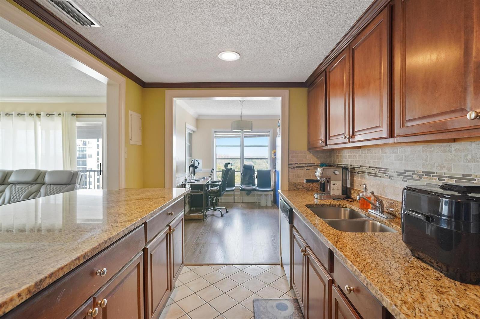 A kitchen with wood cabinets, granite countertops, and a view into an adjacent office space — 4174 Inverrary Drive # 701, Lauderhill FL 33319, LAUDERHILL, FL