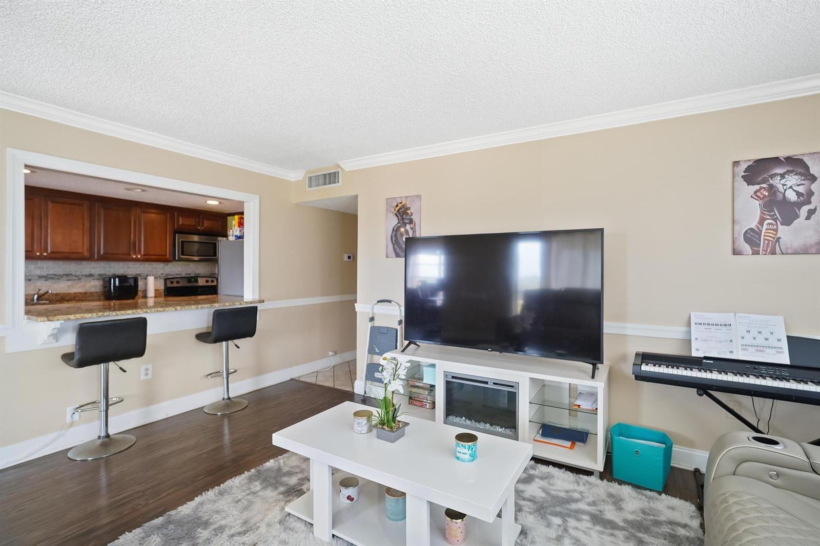 A living room with a television, white media console, coffee table, and kitchen pass-through — 4174 Inverrary Drive # 701, Lauderhill FL 33319, LAUDERHILL, FL