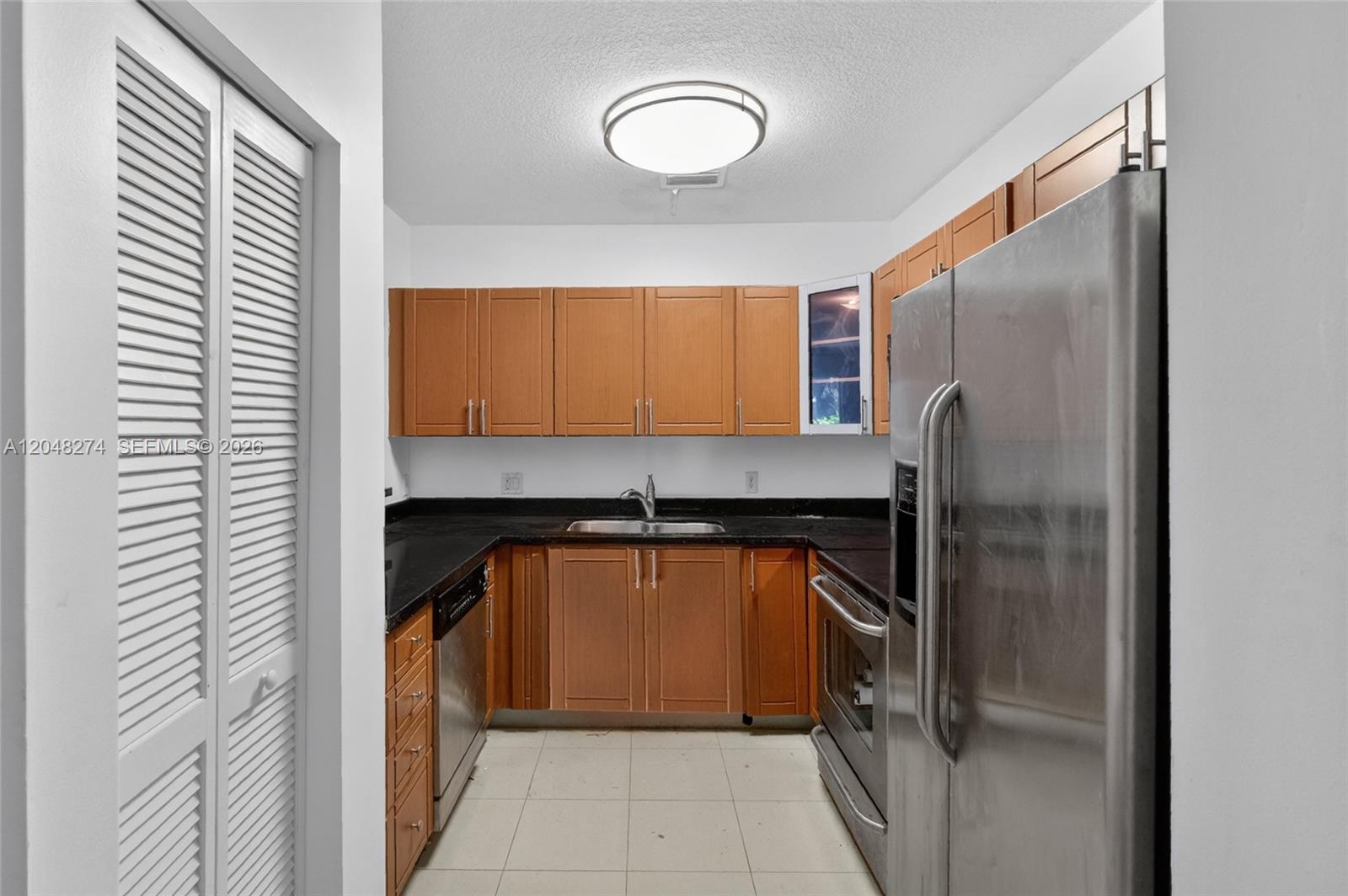 A galley kitchen features wood cabinets, black countertops, and stainless steel appliances — 652 NE 63rd St # 103, Miami FL 33138, MIAMI, FL