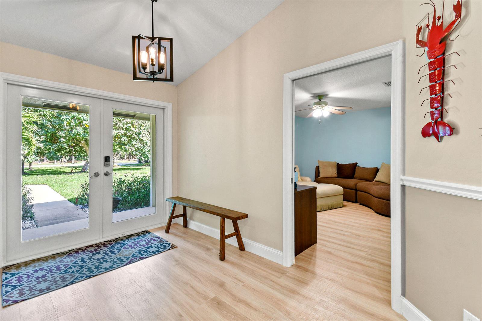 An entryway features light wood flooring, a wooden bench, a patterned rug, and a lobster wall decoration — 17861 Winterhawk Trail, FL 33478, FL