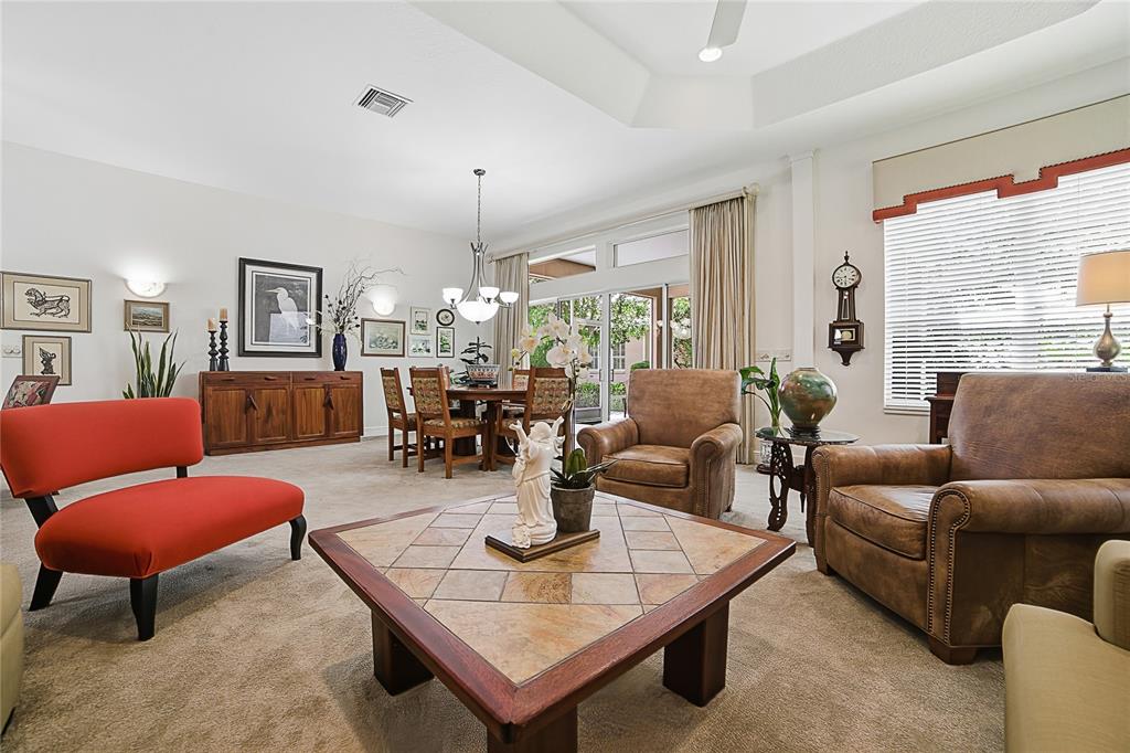 A living room features a tiled coffee table, leather armchairs, a red chair, and dining area — 1832 HARTFORD PATH, THE VILLAGES, FL