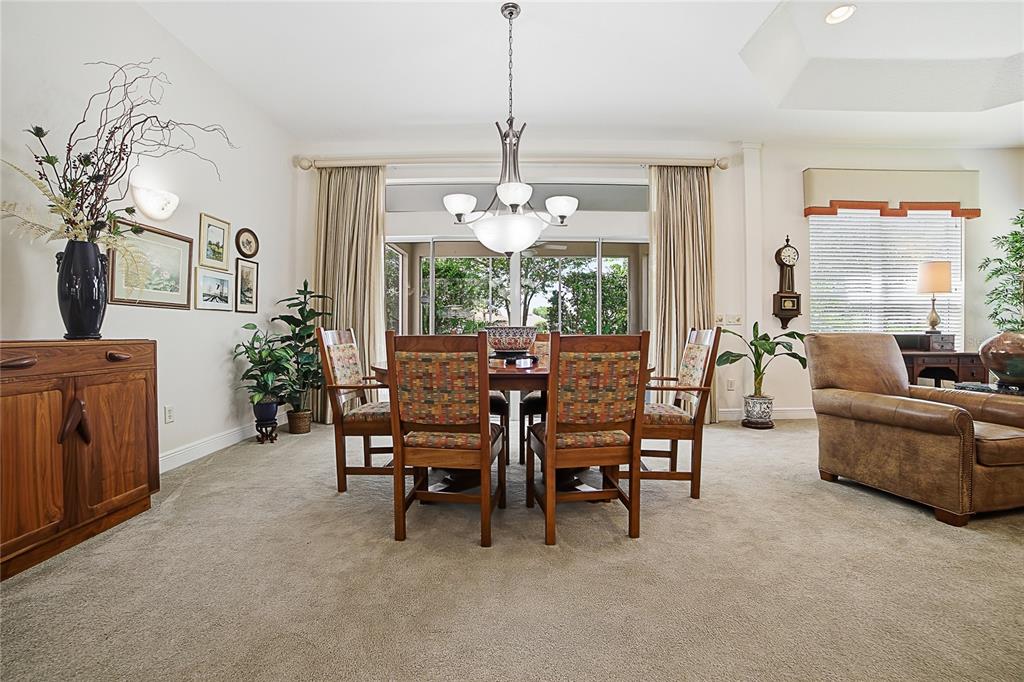 A dining room with a wooden table, patterned chairs, a chandelier, and carpeted flooring — 1832 HARTFORD PATH, THE VILLAGES, FL