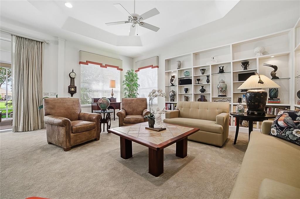 A living room features a tray ceiling, built-in white shelving, and a central coffee table — 1832 HARTFORD PATH, THE VILLAGES, FL