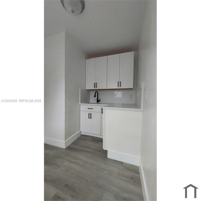 A small kitchen features white cabinets, a sink with a black faucet, and gray flooring — 2927 NW 60th St, Miami FL 33142, MIAMI, FL