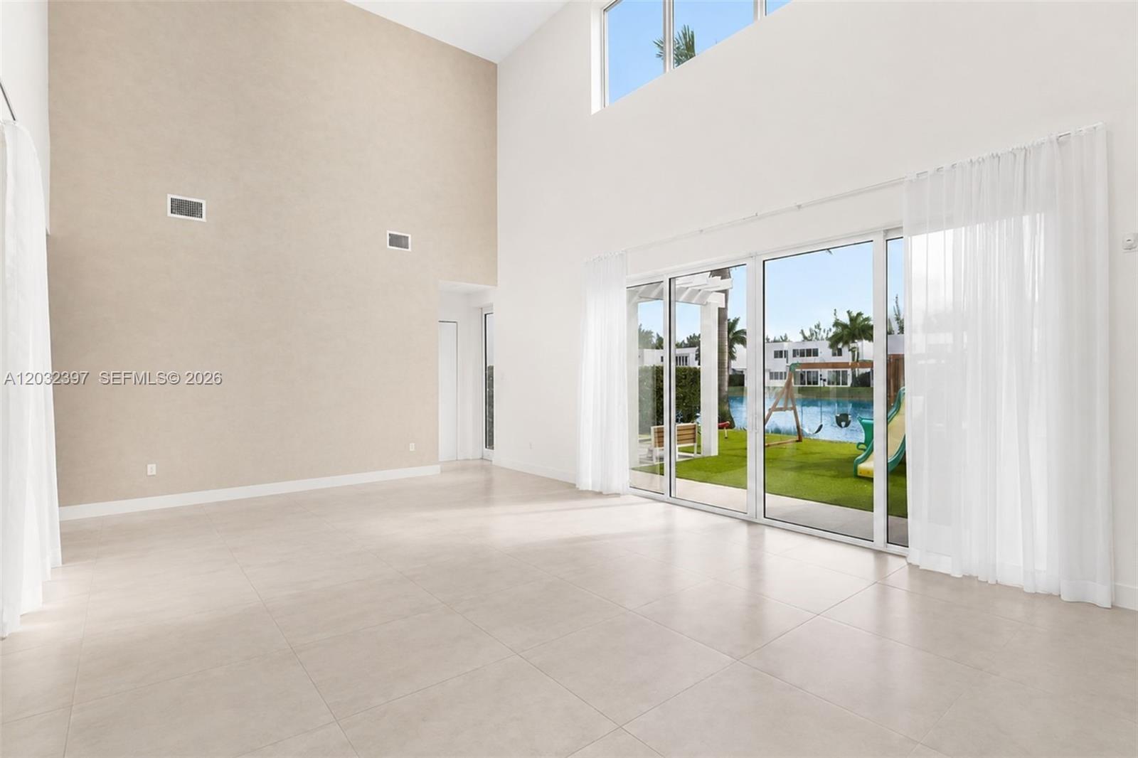 A bright, empty living room features high ceilings, large sliding glass doors, and tile flooring — 10286 NW 75th Ter, Doral FL 33178, DORAL, FL