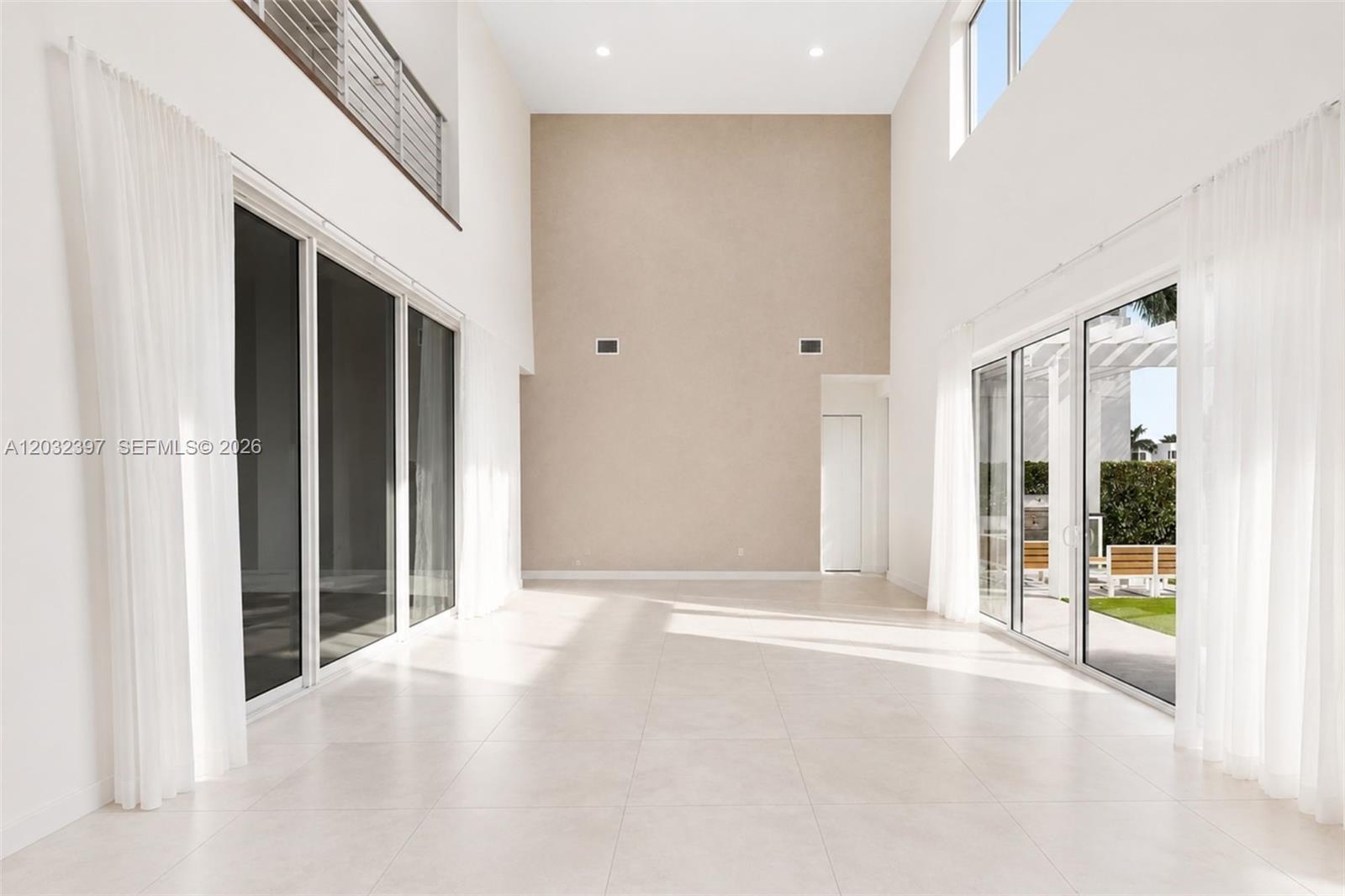 A bright, double-height living room features white tile floors, large glass sliding doors, and curtains — 10286 NW 75th Ter, Doral FL 33178, DORAL, FL