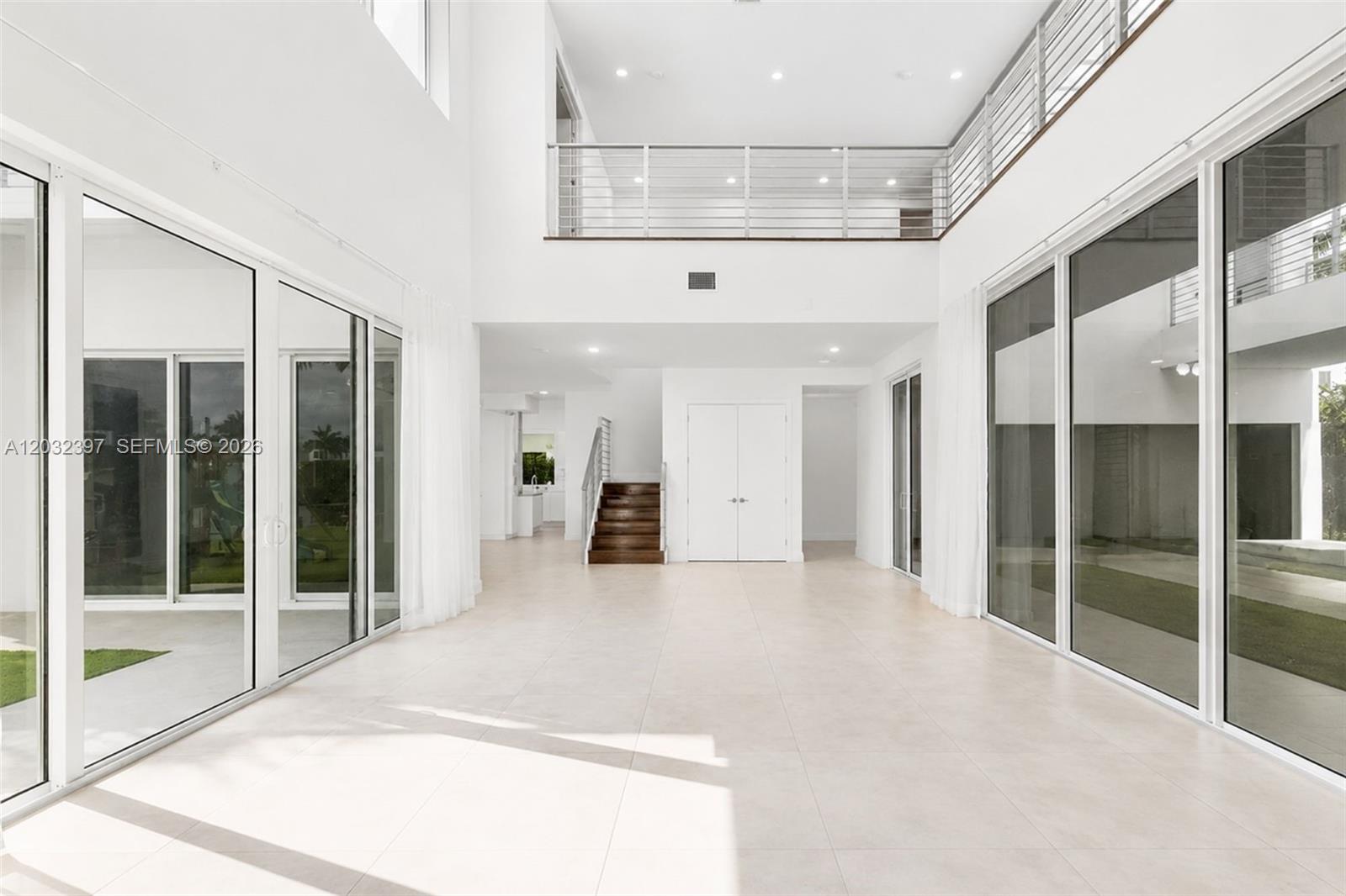 A spacious, minimalist living area features high ceilings, tile floors, and a glass-railed mezzanine — 10286 NW 75th Ter, Doral FL 33178, DORAL, FL