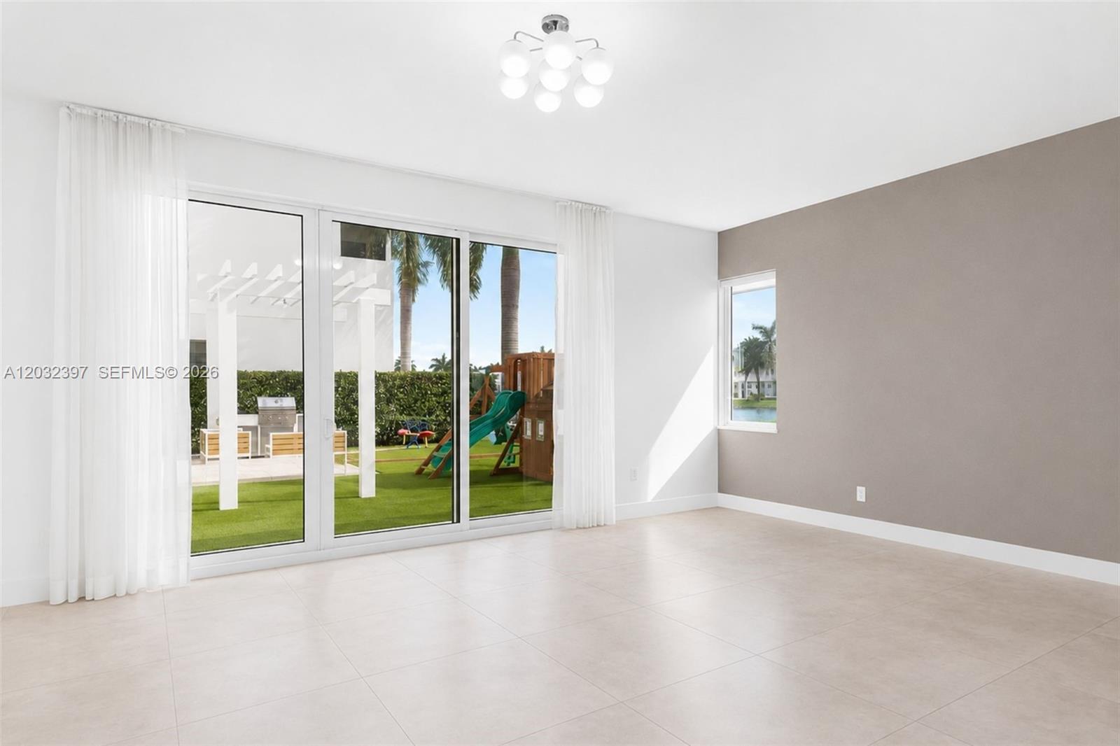 A bright, empty room features large sliding glass doors, light tile flooring, and an accent wall — 10286 NW 75th Ter, Doral FL 33178, DORAL, FL