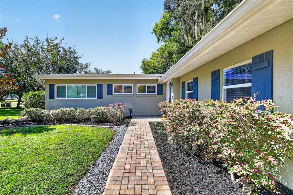 A brick walkway leads to the front entrance of a single-story house with blue shutters — 2434 TRACE AVE, BELLE ISLE, FL