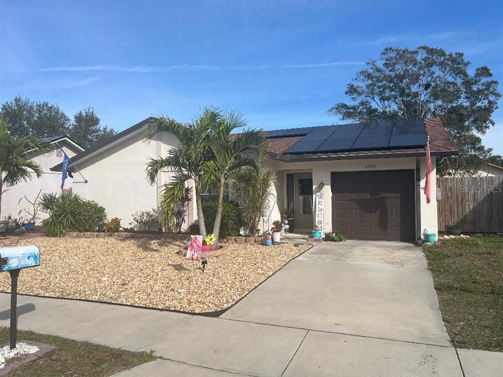 A single-story house with a brown garage door, solar panels, and a gravel front yard — 2009 SAN SEBASTIAN WAY S, CLEARWATER, FL