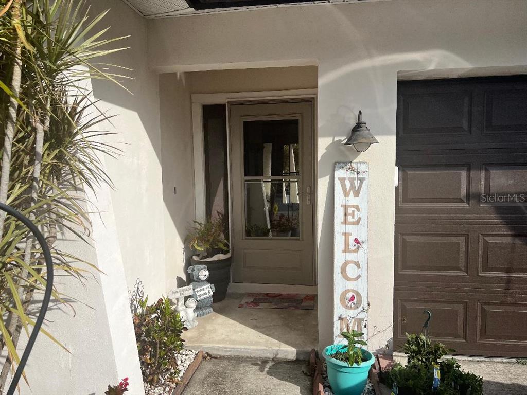 A front entryway features a storm door, a welcome sign, and potted plants — 2009 SAN SEBASTIAN WAY S, CLEARWATER, FL