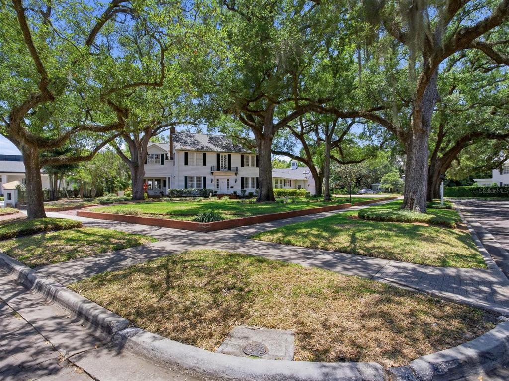 A two-story white house with a brick retaining wall sits behind large oak trees — 3424 JEAN CIRCLE, TAMPA, FL