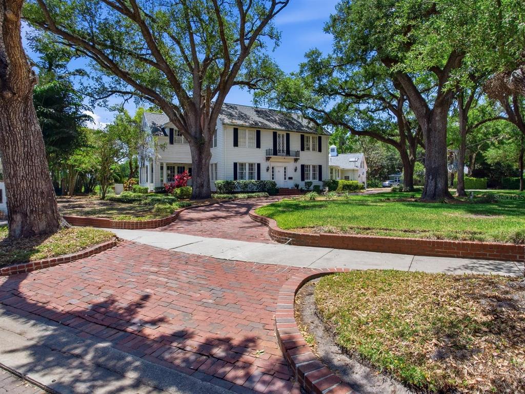 A two-story white house with black shutters sits behind a brick driveway and large trees — 3424 JEAN CIRCLE, TAMPA, FL