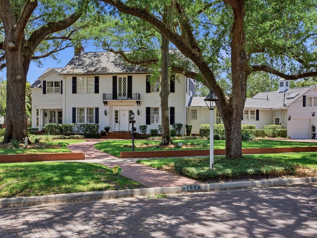 A two-story white house with black shutters sits behind large trees and a brick walkway — 3424 JEAN CIRCLE, TAMPA, FL