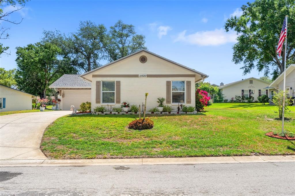 A single-story house with a beige brick facade, brown shutters, and a front lawn — 10520 SPRINGWOOD DRIVE, PORT RICHEY, FL