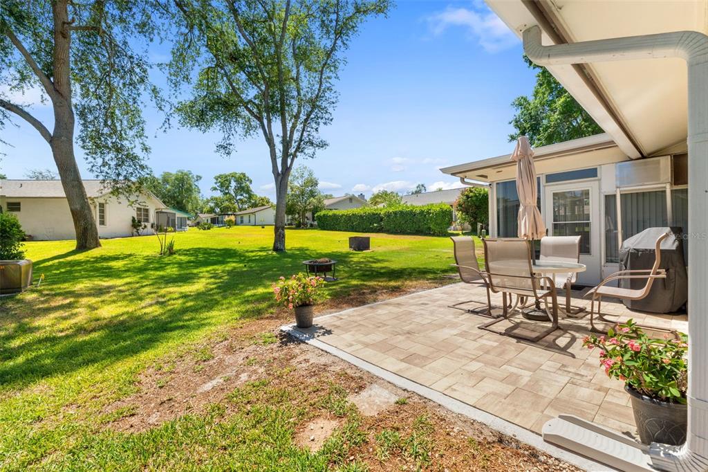A paved patio with outdoor furniture sits beside a house overlooking a large, grassy backyard — 10520 SPRINGWOOD DRIVE, PORT RICHEY, FL