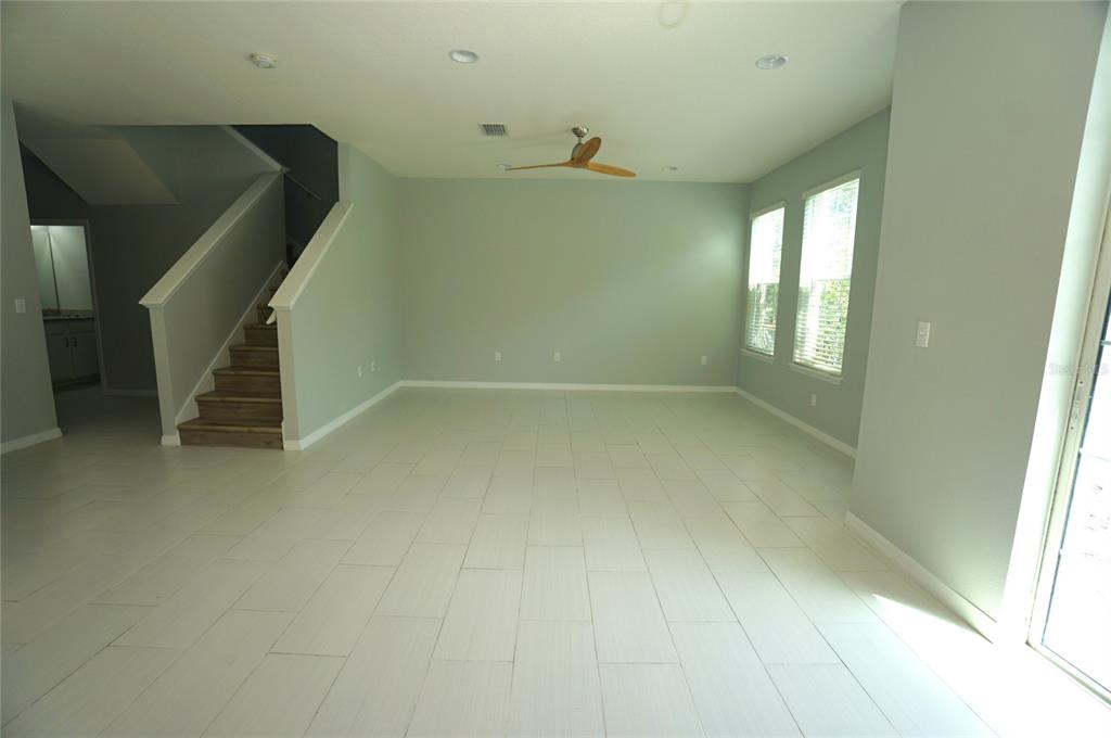An empty living room features light-colored tile flooring, a ceiling fan, and a wooden staircase — 7001 INTERBAY BOULEVARD UNIT 236, TAMPA, FL