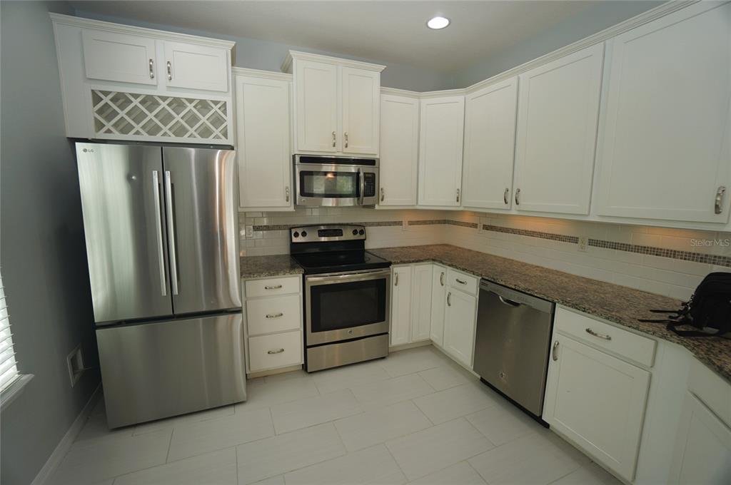 A kitchen features white cabinets, stainless steel appliances, granite countertops, and a tiled backsplash — 7001 INTERBAY BOULEVARD UNIT 236, TAMPA, FL