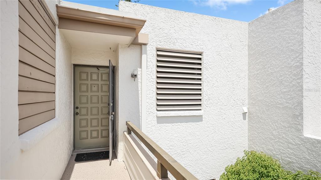 An exterior view of a building entrance with a textured white wall and louvered shutters — 303 SPRINGDALE DRIVE UNIT 303, BRADENTON, FL