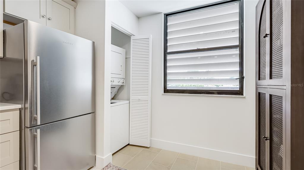 A kitchen area features a stainless steel refrigerator, a stacked washer-dryer, and a louvered window — 303 SPRINGDALE DRIVE UNIT 303, BRADENTON, FL